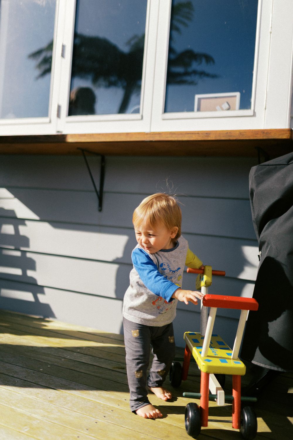 Young child exploring on an outdoor deck with a toy chair.