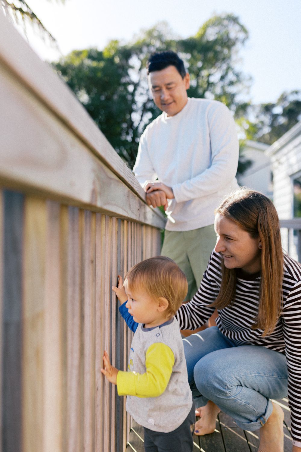 Family members playing together on an outdoor deck with sunlight filtering through trees.