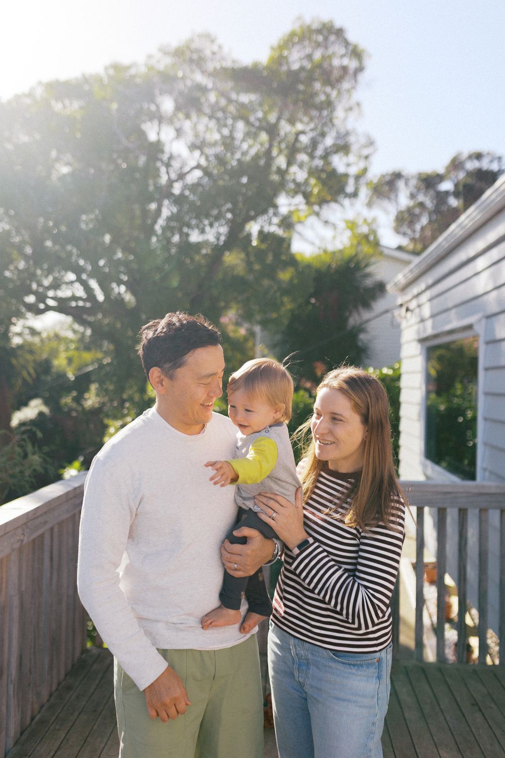A happy family shares joyful moments together on a sunny deck with trees in the background.