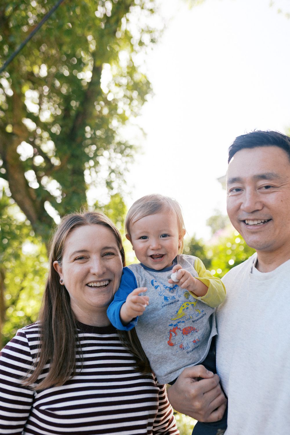 Natural light illuminates a cheerful family portrait series against a leafy backdrop.