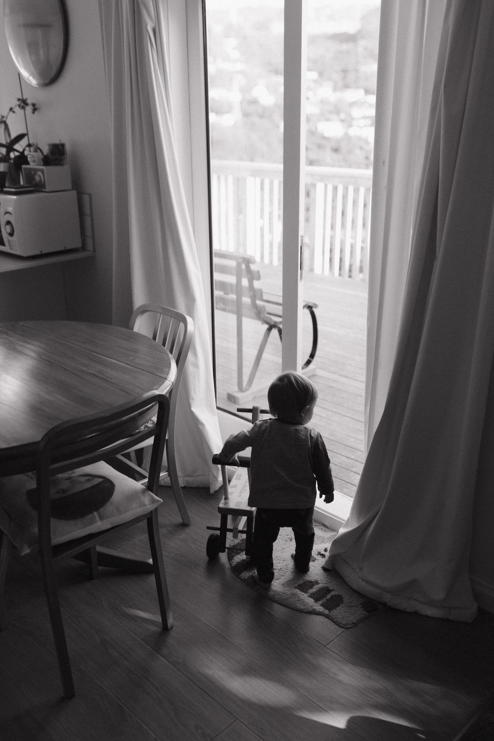 A sequence of black and white photos showing a small child playing behind sheer curtains in morning light.