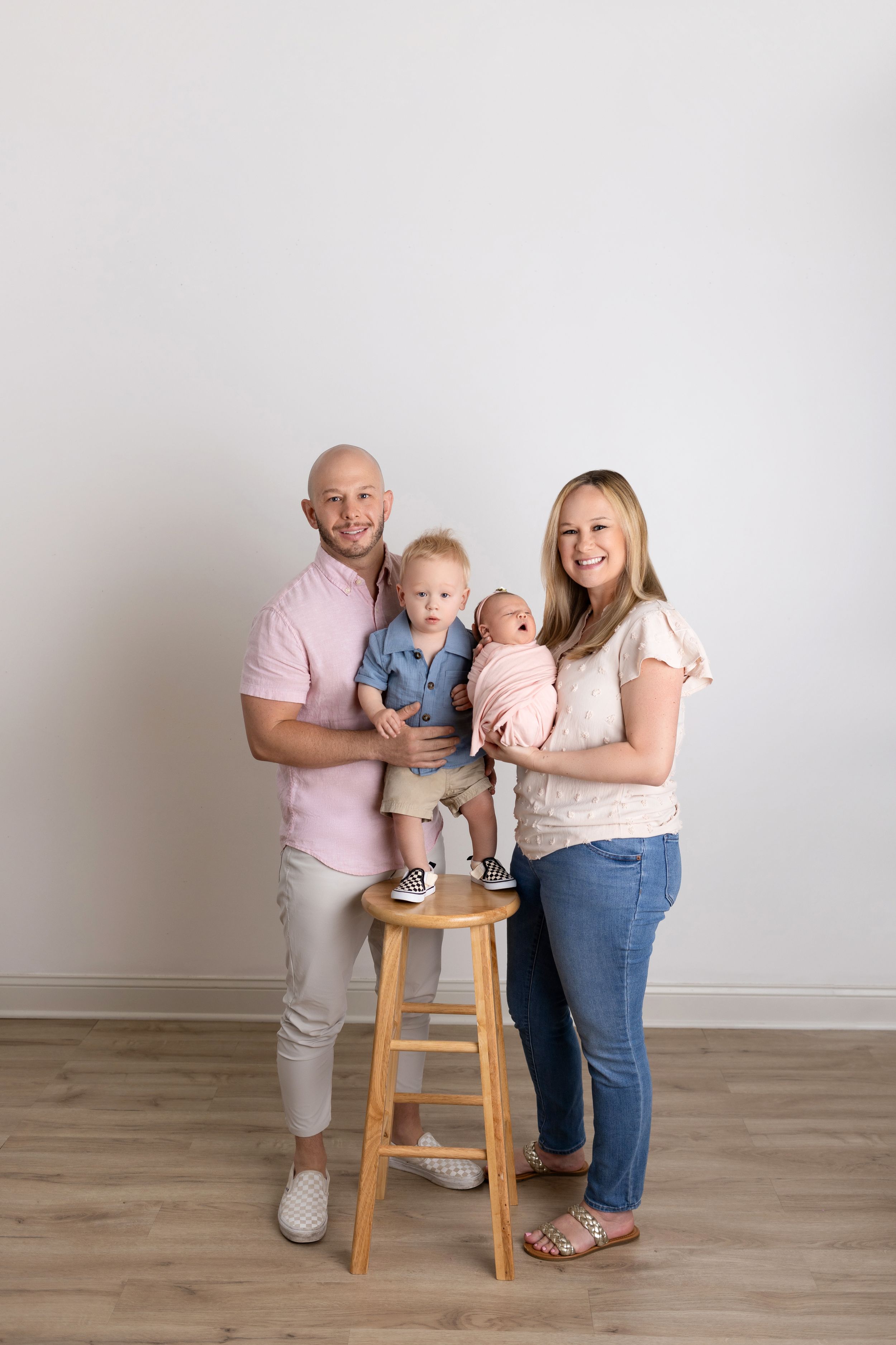 Family portrait session showing tender moments with baby on wooden stool against neutral studio backdrop.