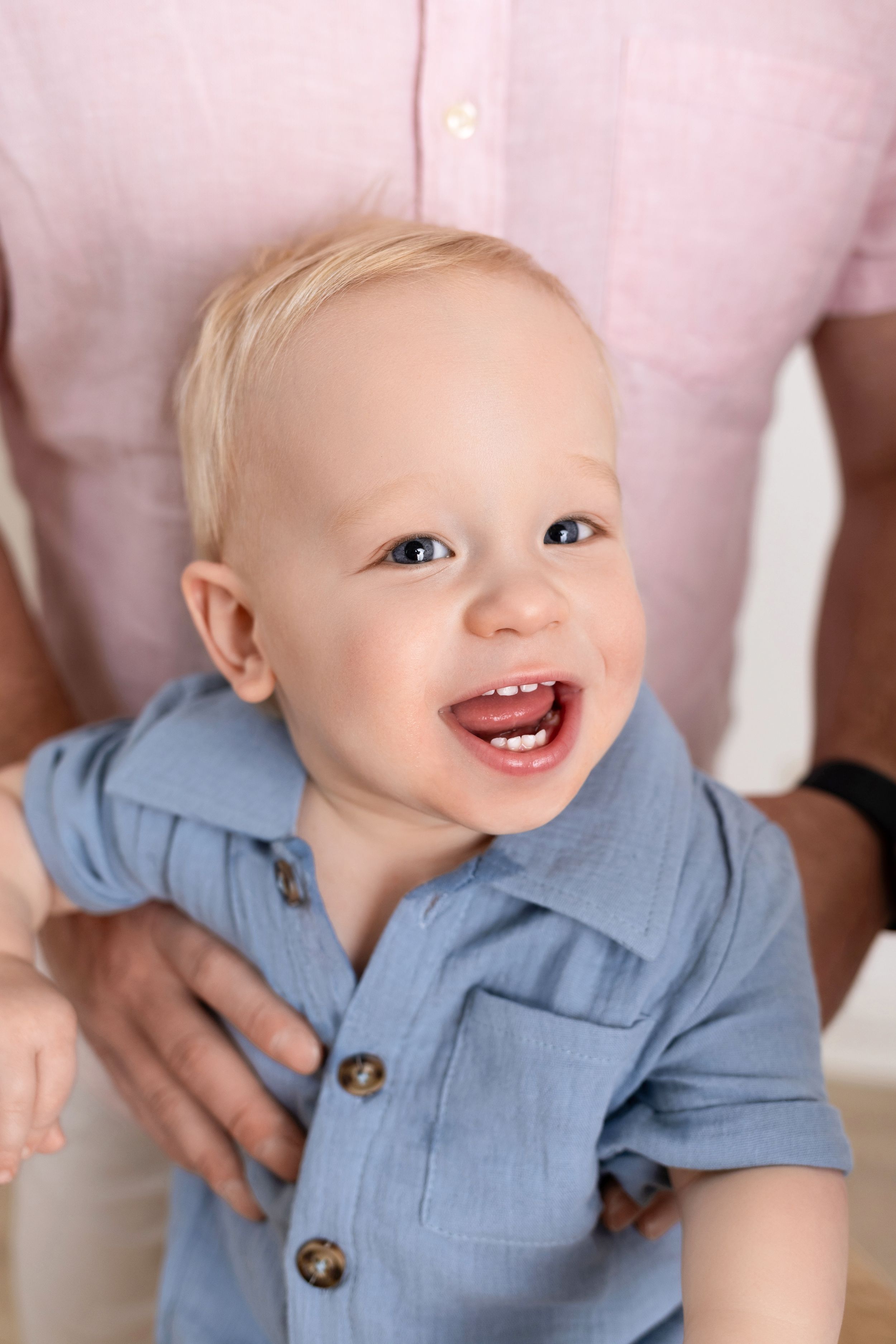 A baby in a light blue collared shirt smiles joyfully in a series of candid photos.