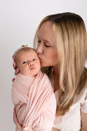 A series of tender moments between a parent and swaddled baby in pink against a white backdrop.