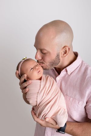 Sweet moments captured of a parent cuddling and kissing a baby wrapped in soft pink.