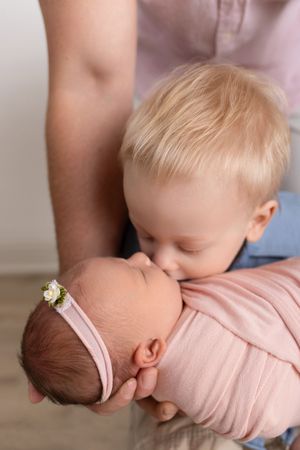 Tender side view portraits showing siblings bonding with a newborn baby wrapped in pink.
