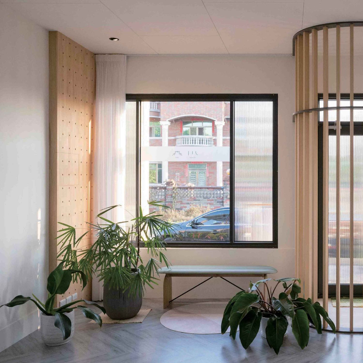 Contemporary office interior with wooden slat divider, potted plants, and windows creating a bright, minimalist workspace.