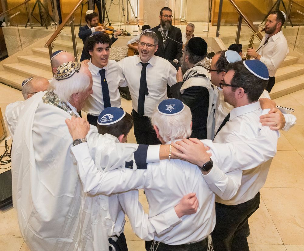 Jewish wedding celebration with guests dancing in a circle during traditional hora dance at an indoor venue.
