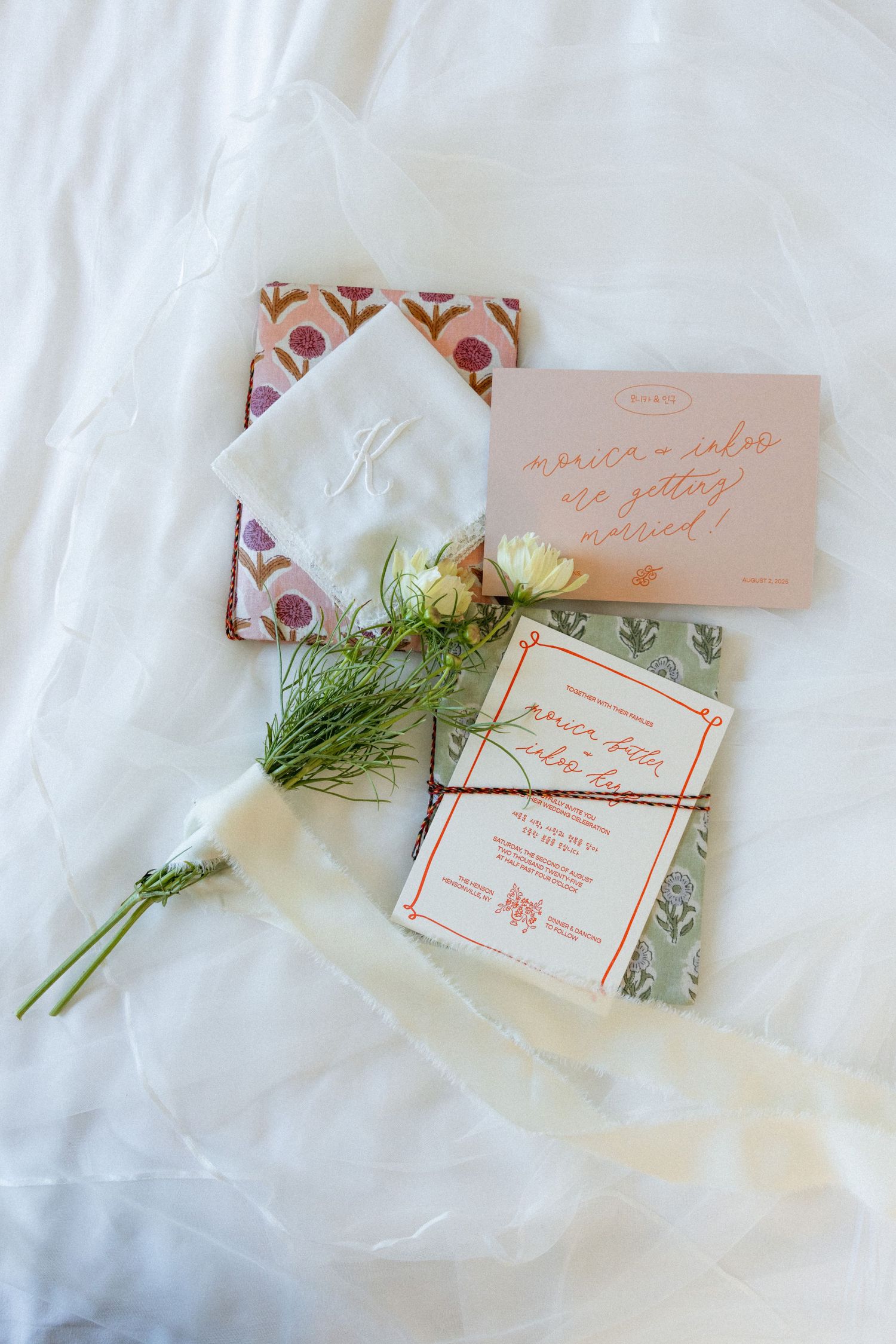 Wedding invitation suite with floral designs and greenery on white fabric.