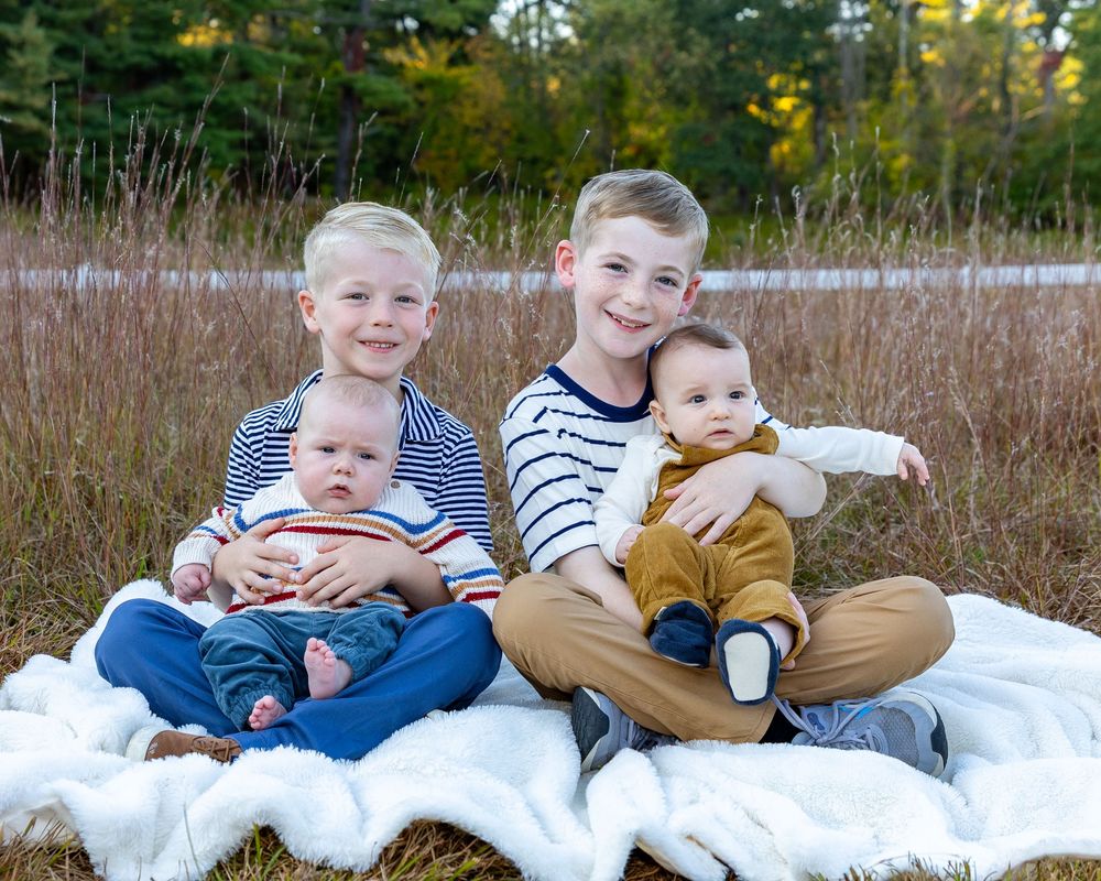 Cousins pose together in a grass field outdoors during autumn with fall foliage in background in Sudbury, MA outside Boston.