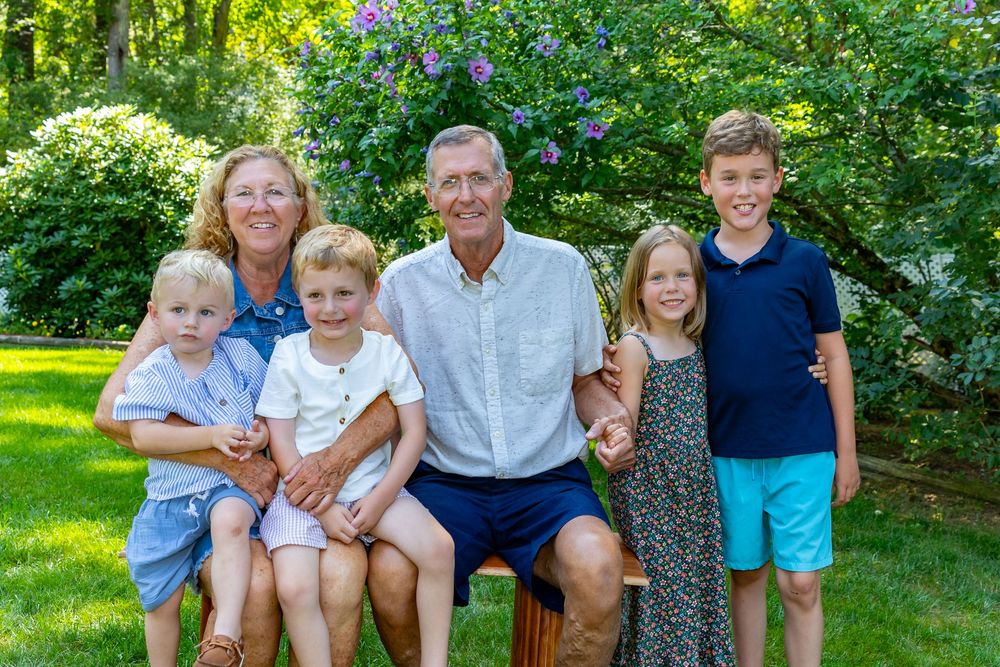 Grandparents & grandchildren pose in a lush garden setting with green trees and flowers during an extended family photo session in Acton, MA