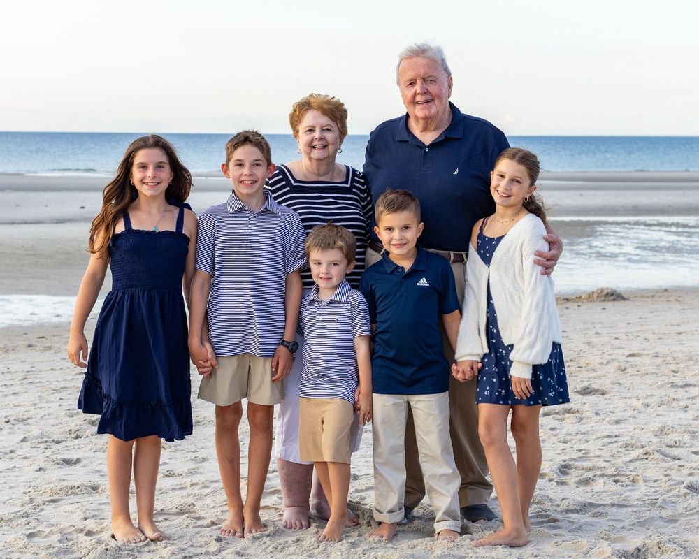 Grandparents & grandchildren stand together on a sandy beach with ocean waves at Chapin Beach Dennis, MA during extended family photos.