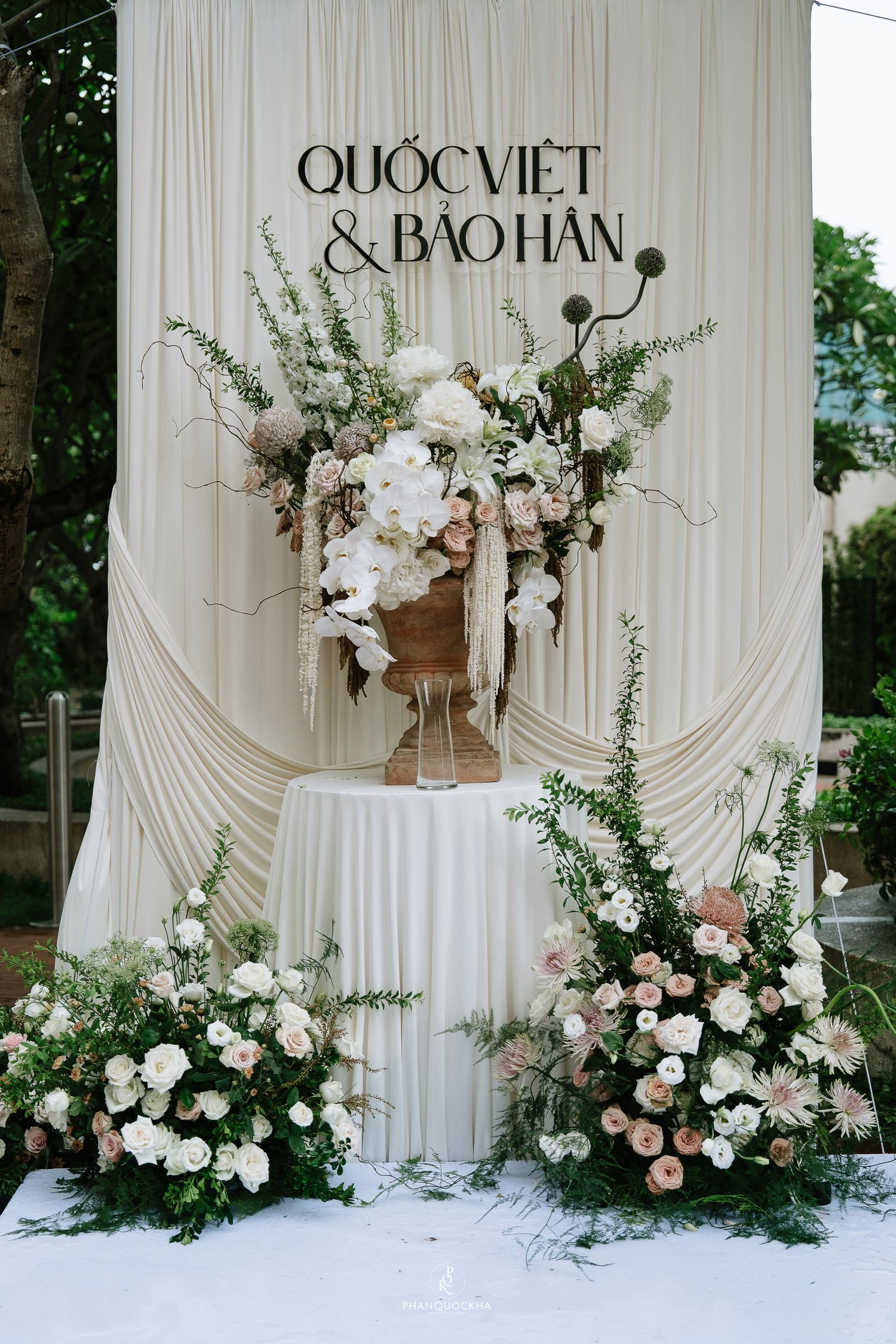 White draped wedding backdrop with lush floral arrangement for Quoc Viet and Bao Han ceremony.