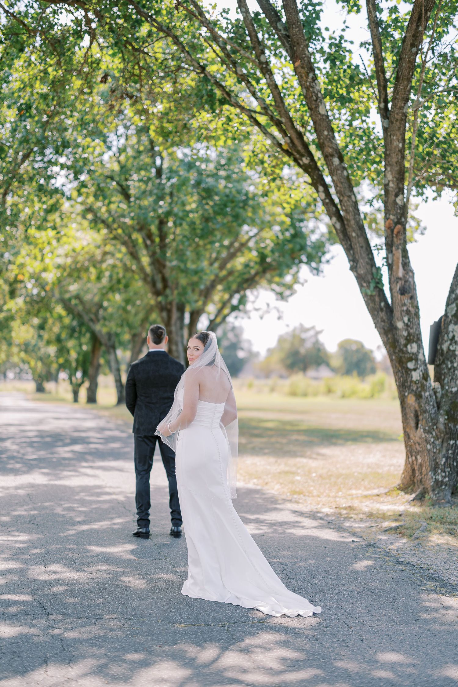 A couple in wedding attire walking down a tree-lined path together on their special day.