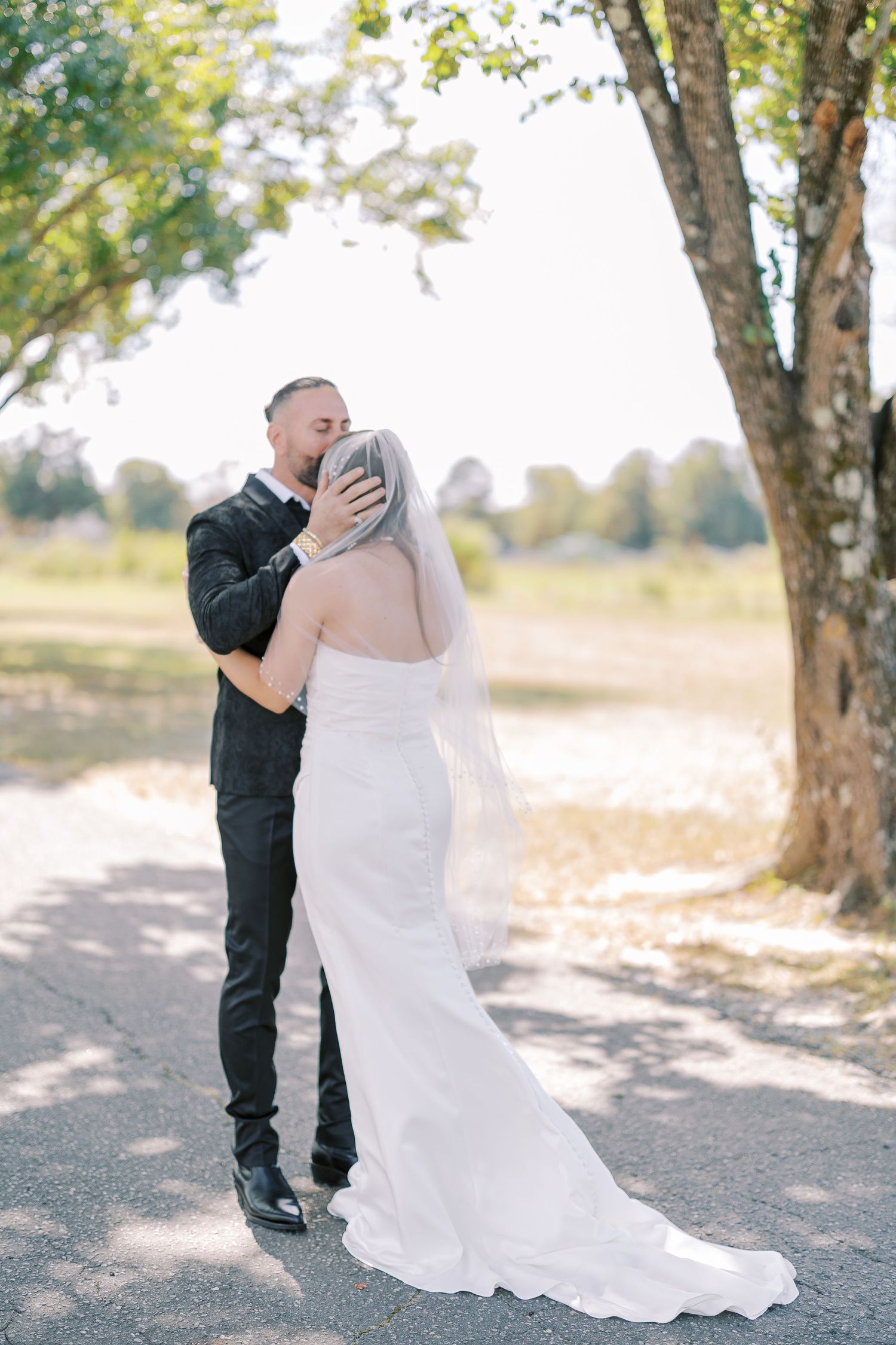 Dancing couple surrounded by trees cast romantic shadows in dappled sunlight during outdoor photo session.