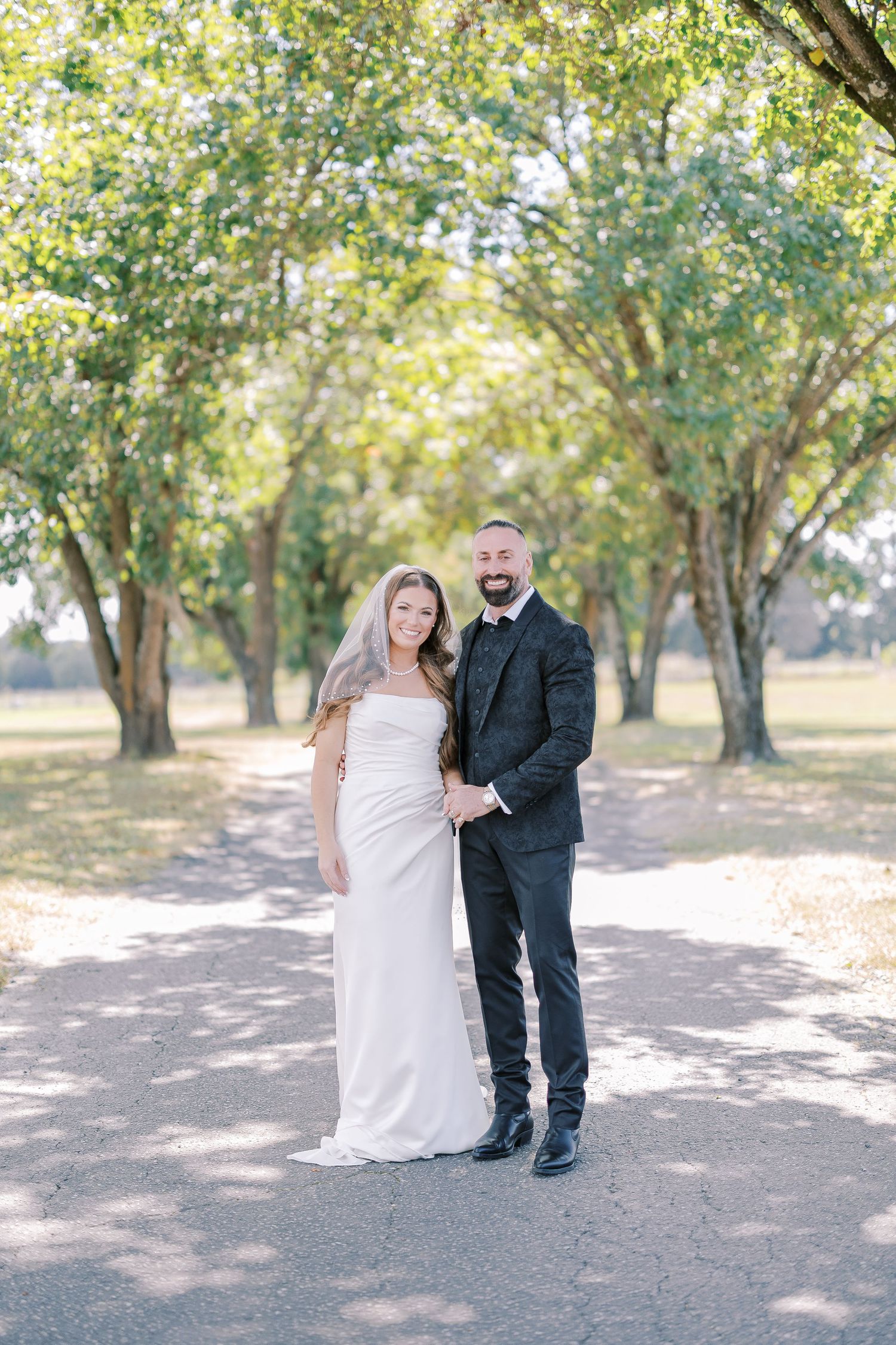 A wedding photo series showing a small child in formal attire standing with a bride under sun-dappled trees.