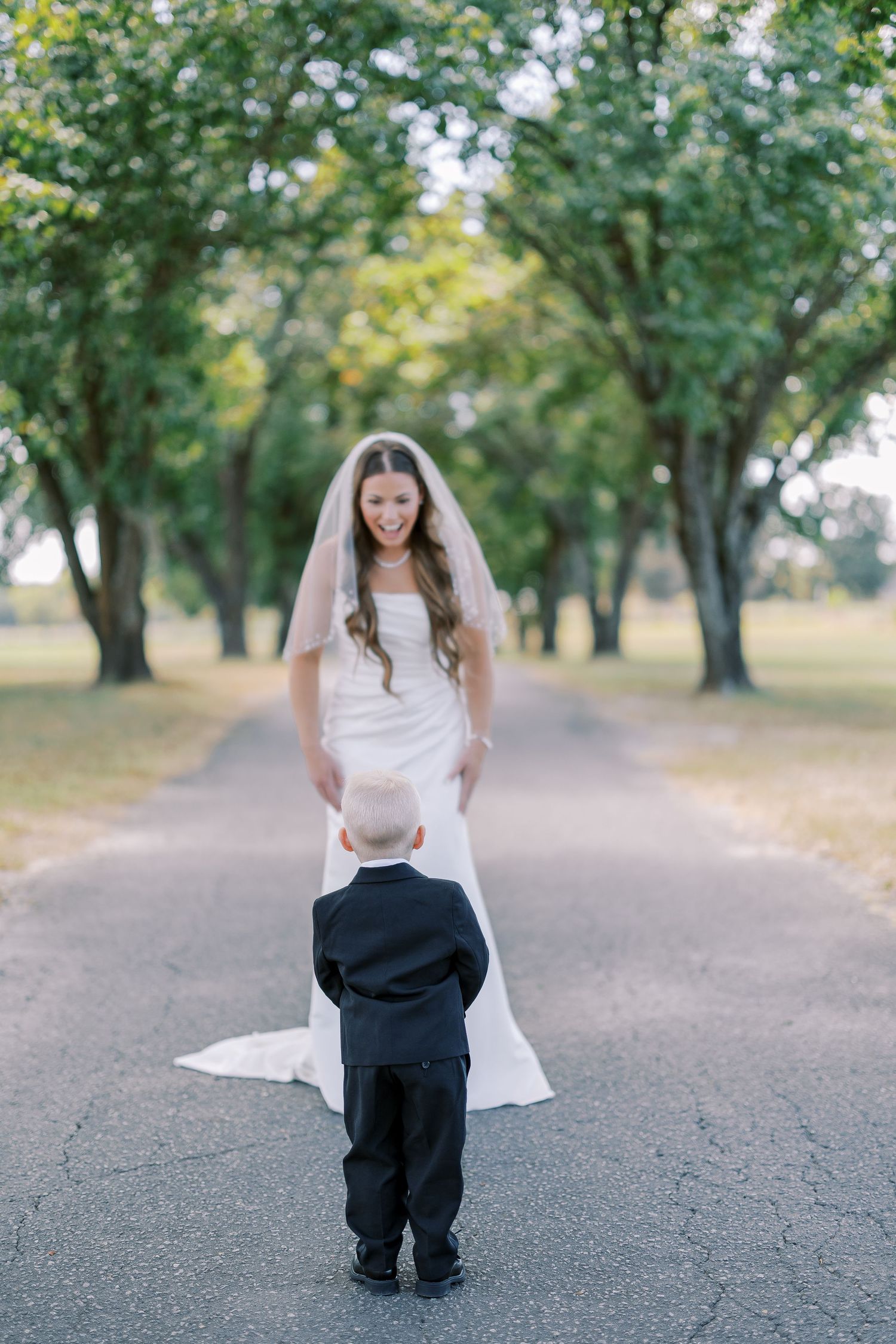 A touching moment between a small child and bride on a quiet tree-lined path during a wedding.