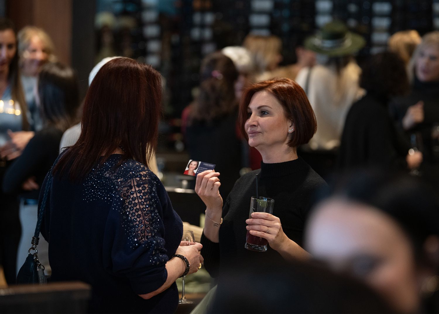 Two women holding drinks and conversing at a networking event.