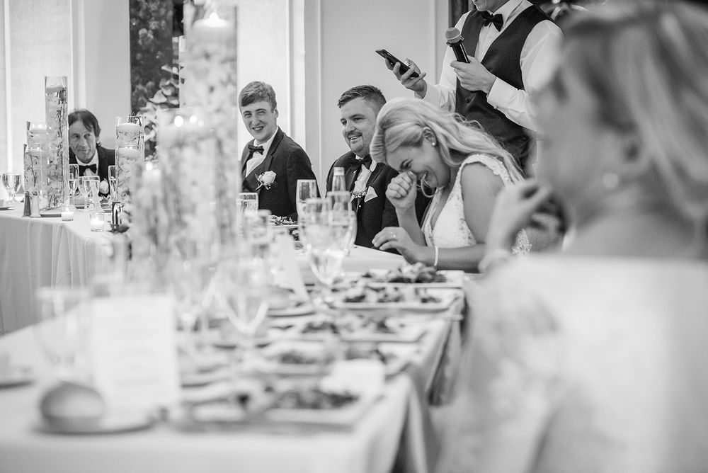 A black and white wedding reception candid showing guests seated at tables enjoying conversation and celebration.