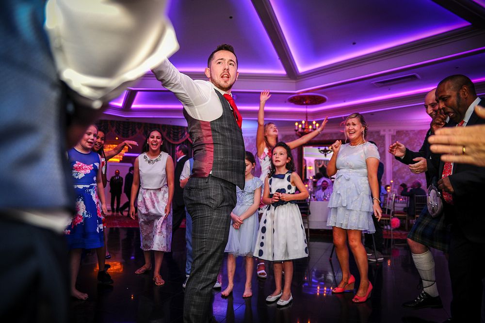 Wedding reception guests dancing on a purple-lit dance floor during an evening celebration.