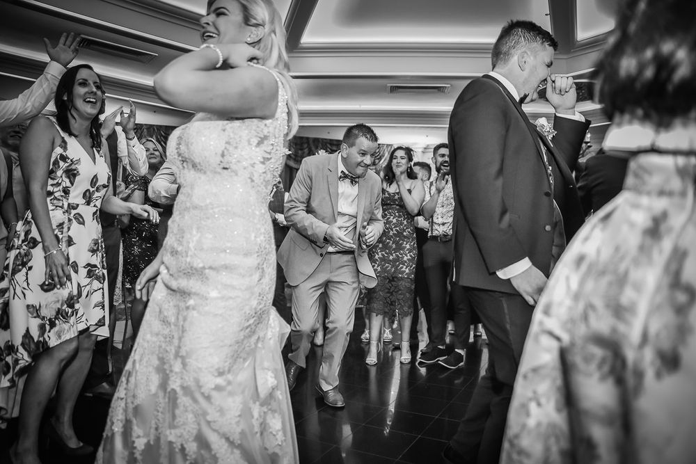 A wedding party dances joyfully together on an outdoor patio during the evening reception celebration.