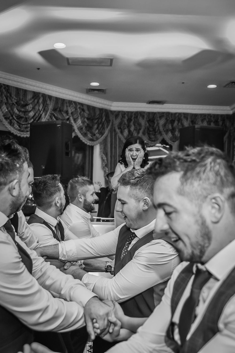 A black and white photo of groomsmen linking arms and swaying together during a wedding celebration.