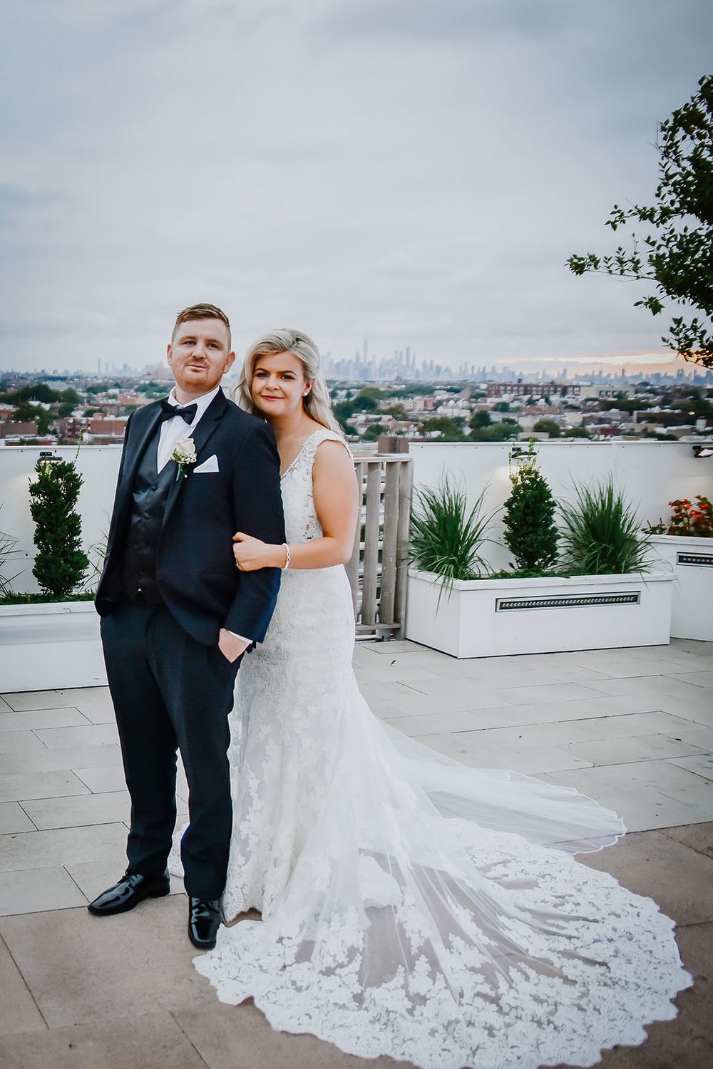 Wedding couple poses on rooftop terrace with city skyline view at outdoor venue during celebration.