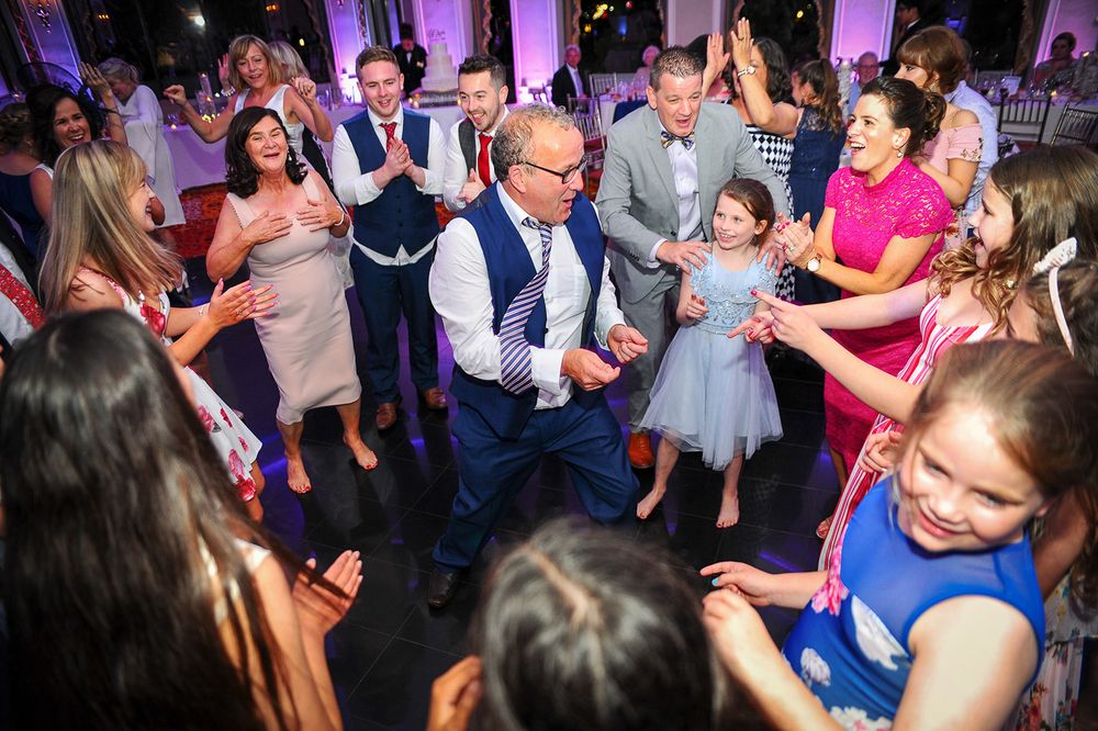 Wedding guests dance together on the illuminated dance floor surrounded by purple uplighting at an elegant reception.
