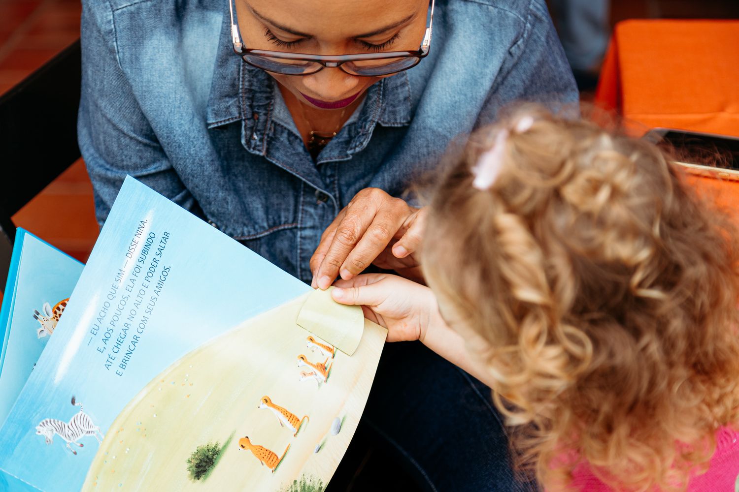 An adult and young child read a picture book together while seated, focused on sharing a story.