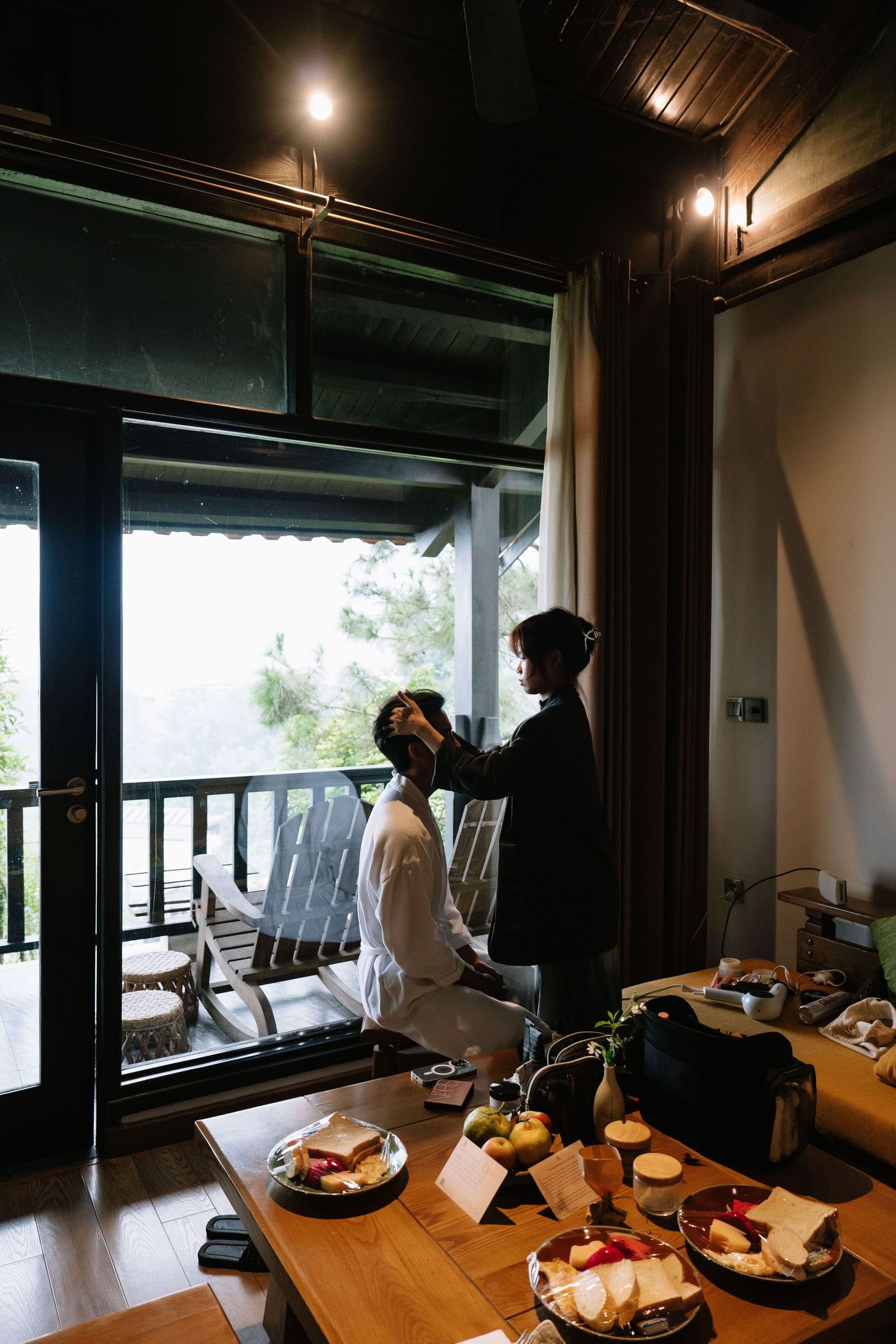 Bride getting hair styled near balcony window with mountain view and breakfast spread.
