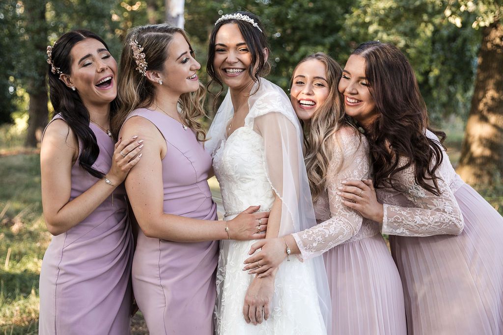 Bride and bridesmaids hugging and laughing together in the gardens of Kelham House