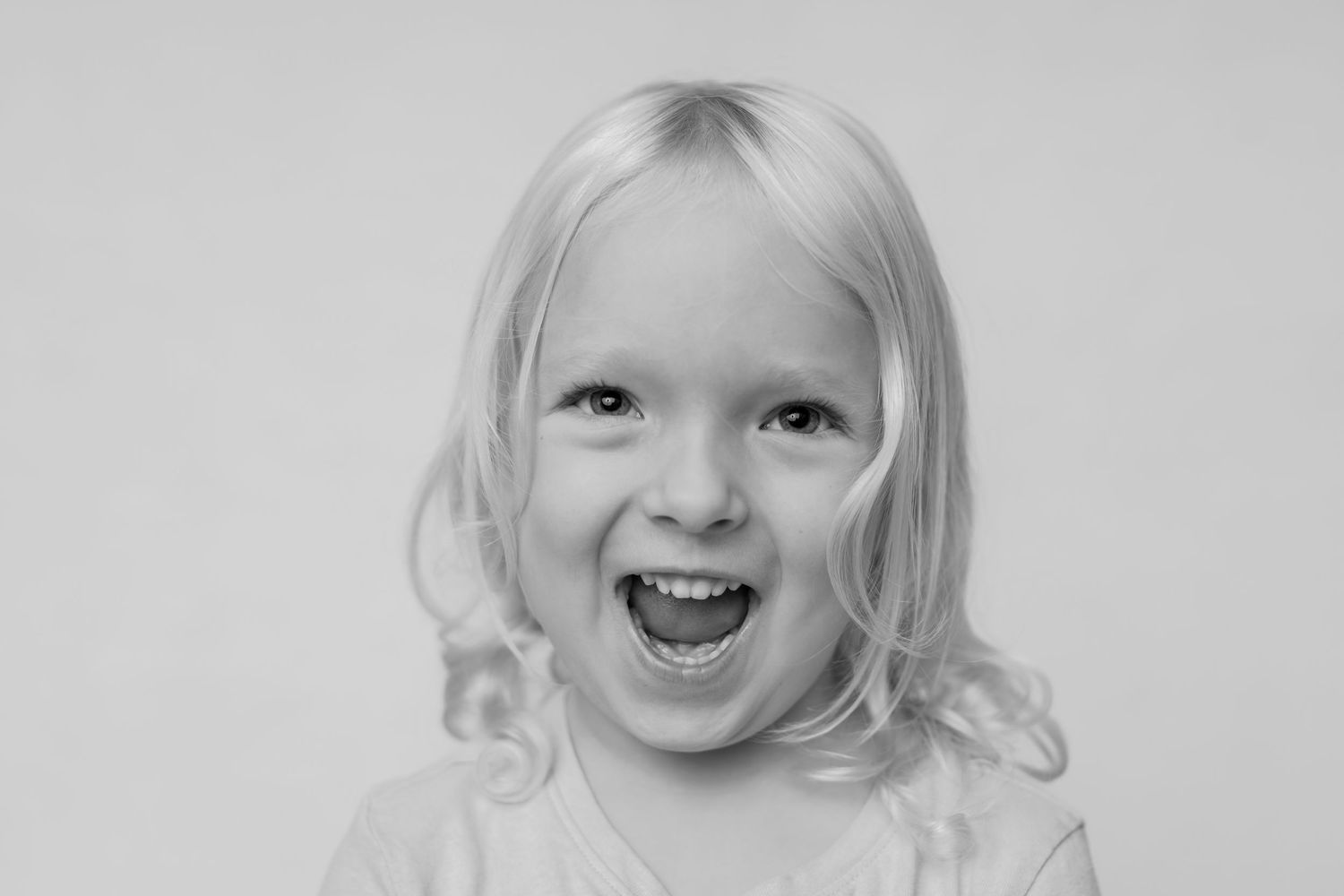 Black and white portrait of a joyful child with blonde curly hair.