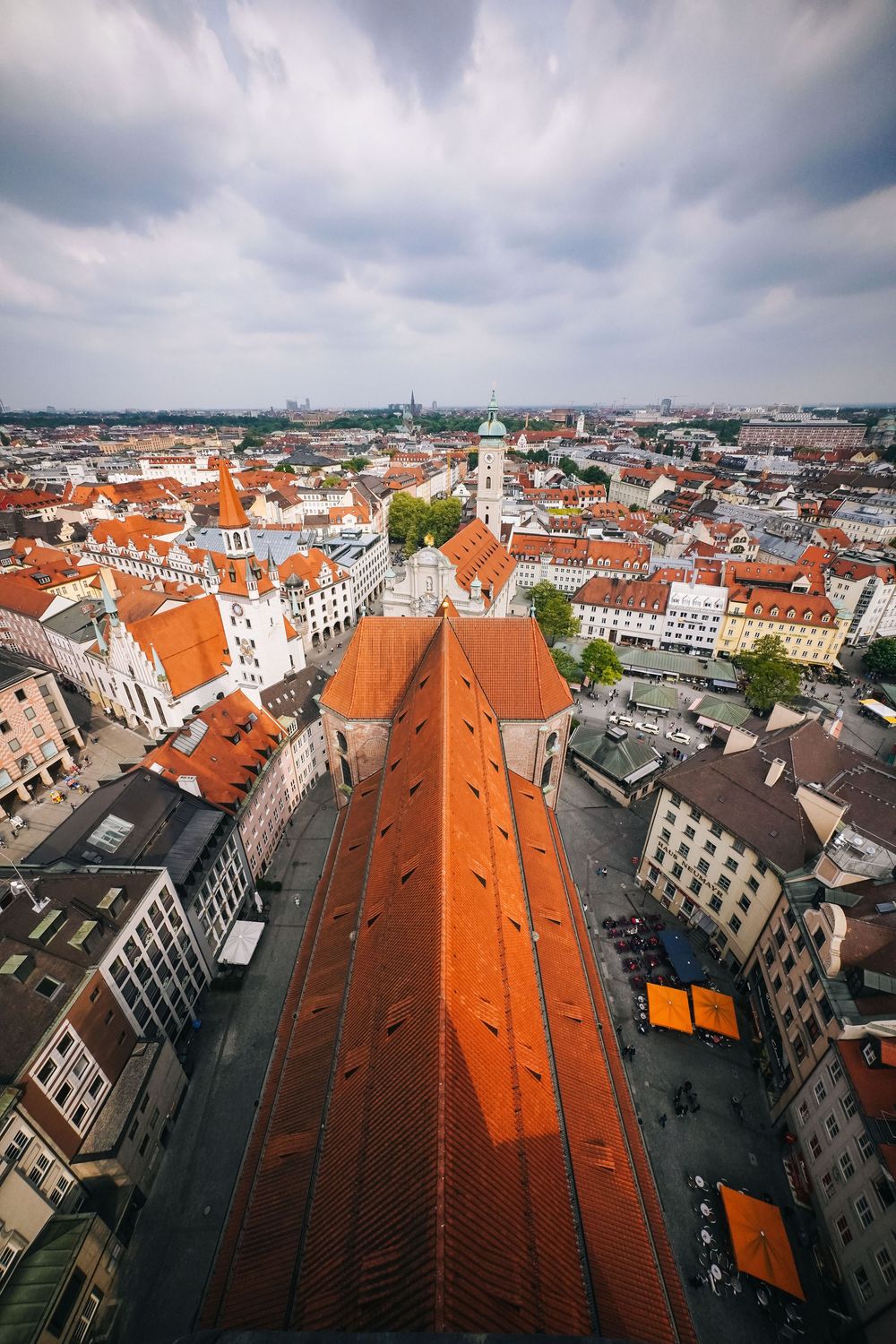 Panoramic aerial view of orange terracotta rooftops and historic buildings in a European city center on a cloudy day.