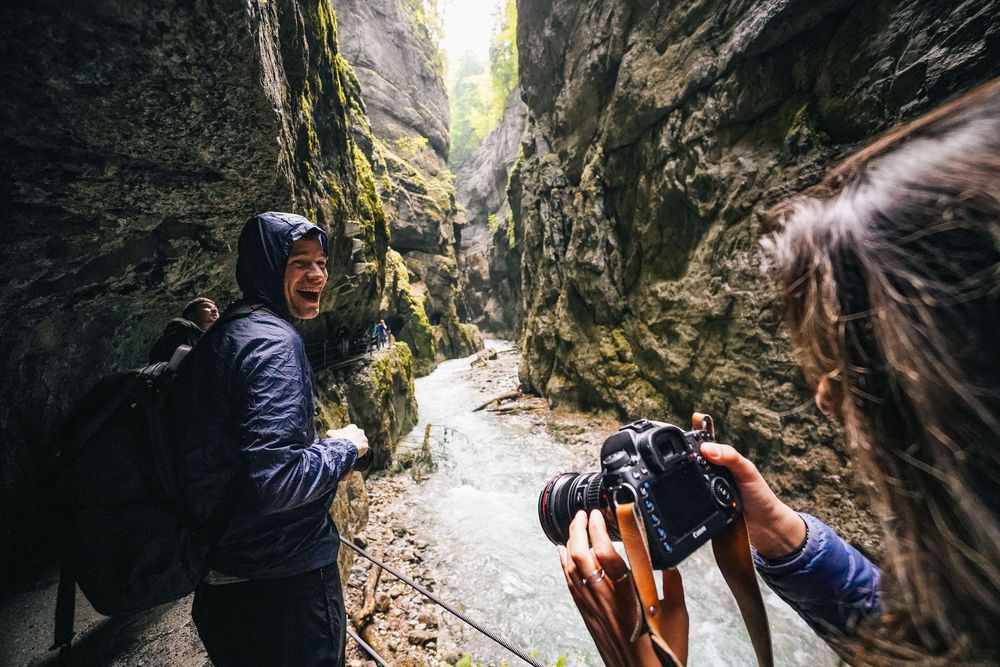 Hikers explore a narrow, rocky canyon trail with steep moss-covered walls and natural light filtering from above.