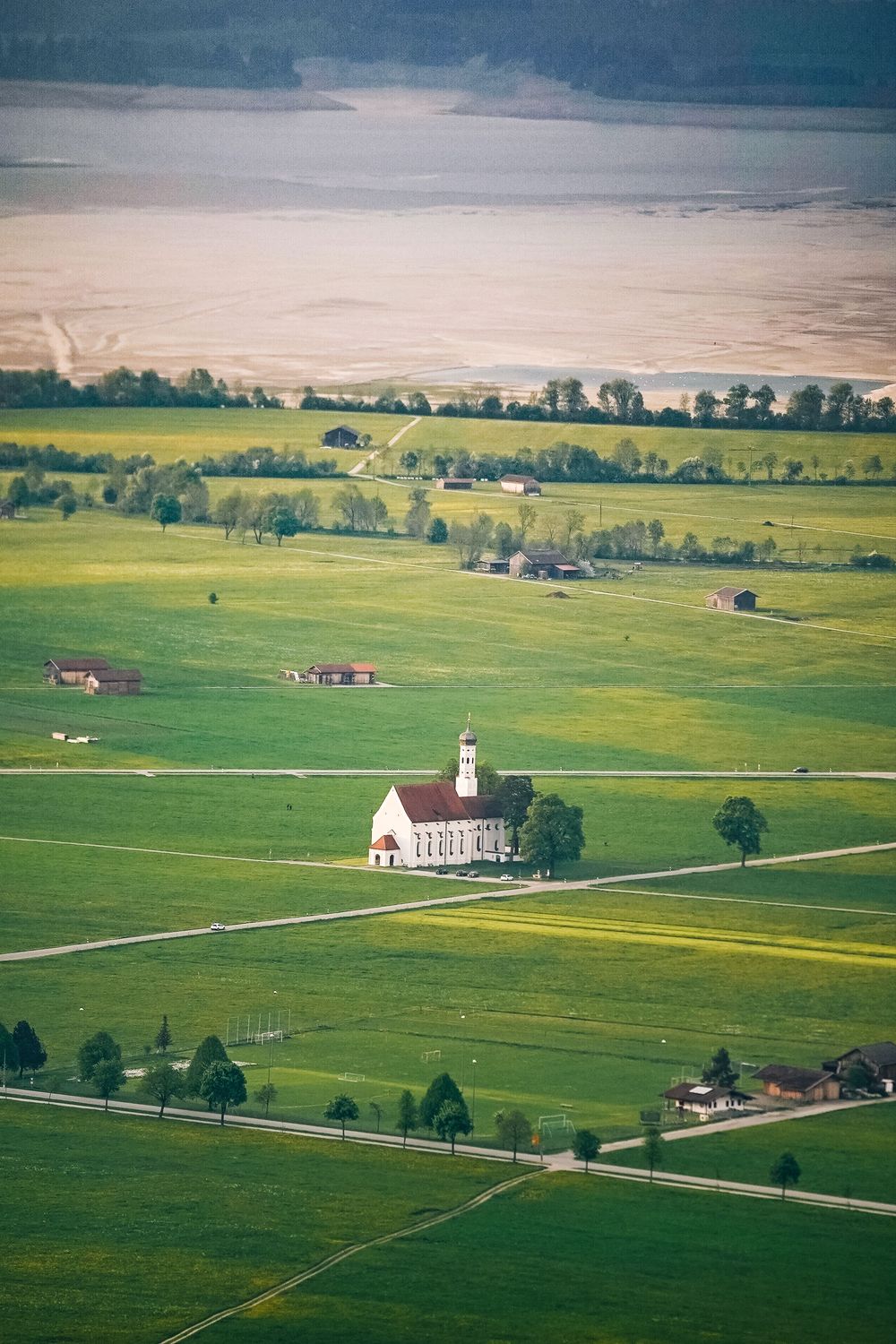 Aerial view of a rural landscape with churches and farm buildings scattered across green rolling meadows.