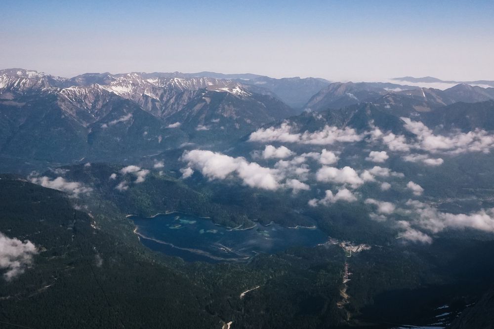 Aerial view of snow-capped mountain peaks with scattered clouds and a winding river valley below.