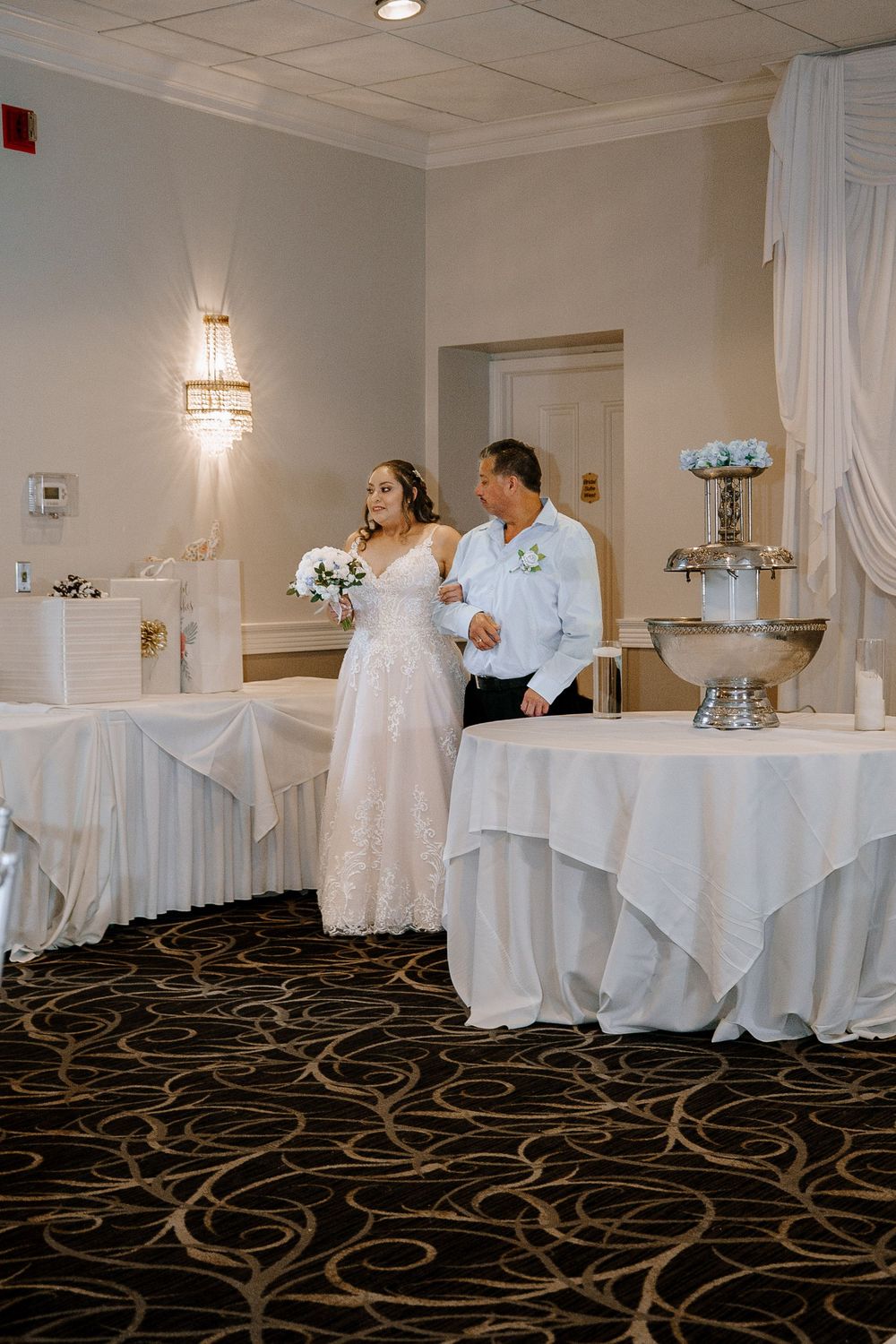 Wedding reception venue with elegant white tablecloths and dark patterned carpet in a banquet room layout.
