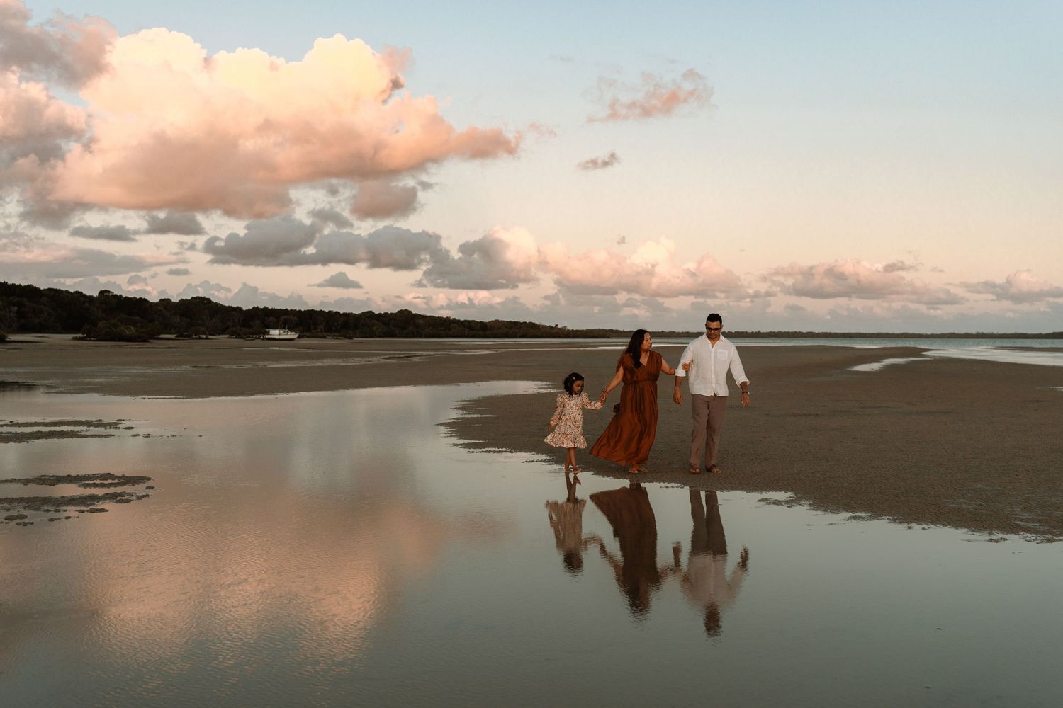People walking on a serene beach at sunset with reflections in the shallow water creating a mirror-like effect.