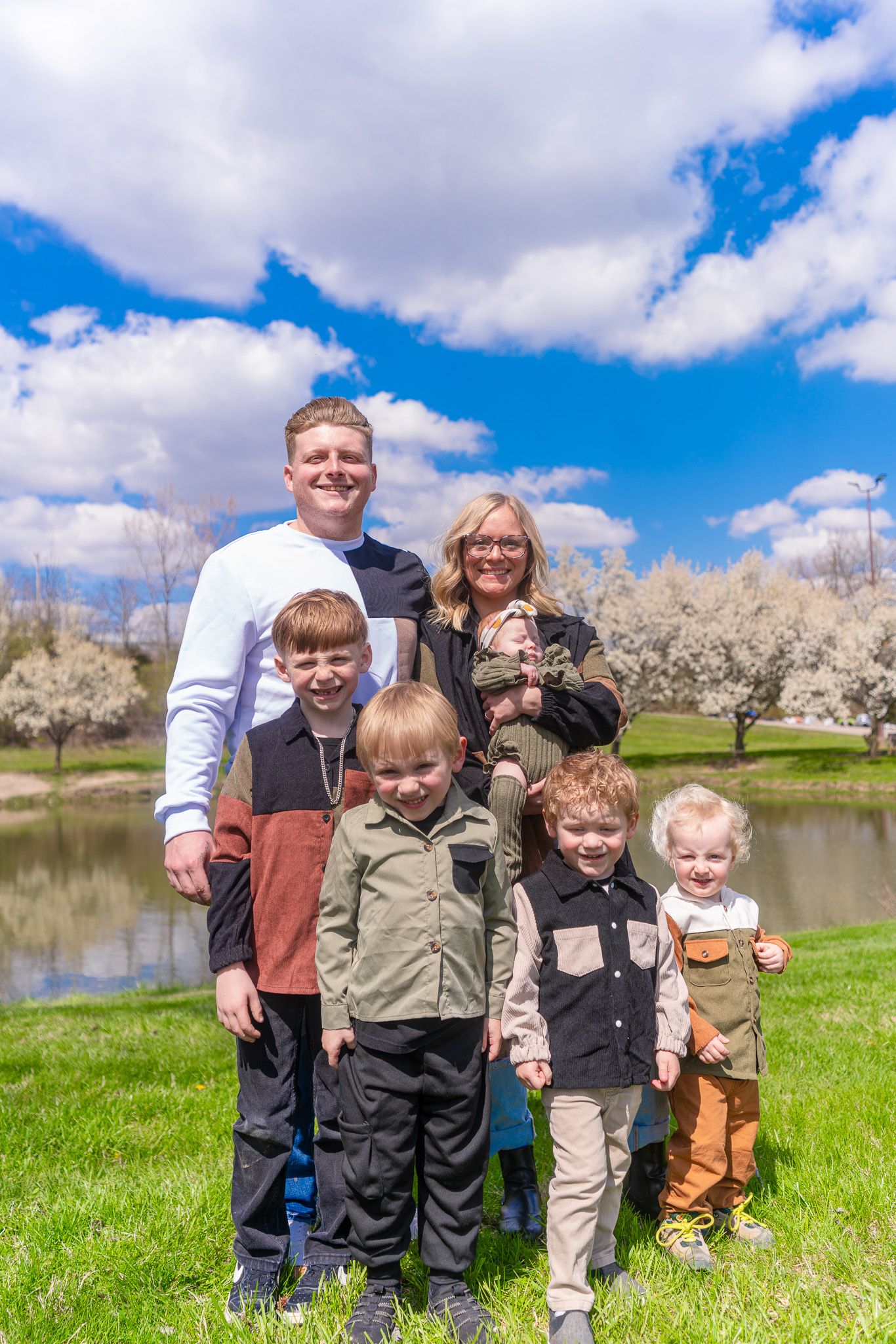 Group photo on green grass with pond and blooming trees in background on sunny spring day.