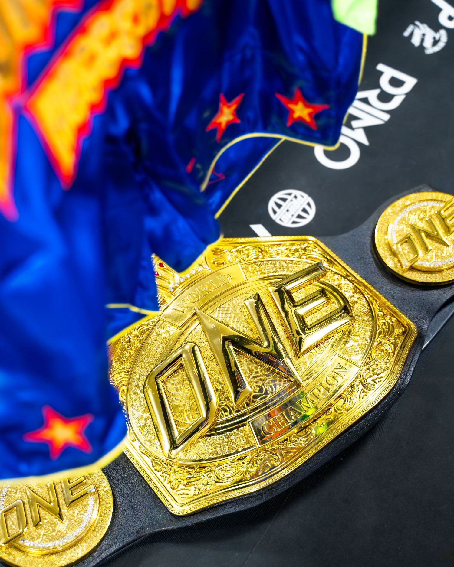 Shiny gold UFC championship belt displayed against dark background with blue and red lighting effects.
