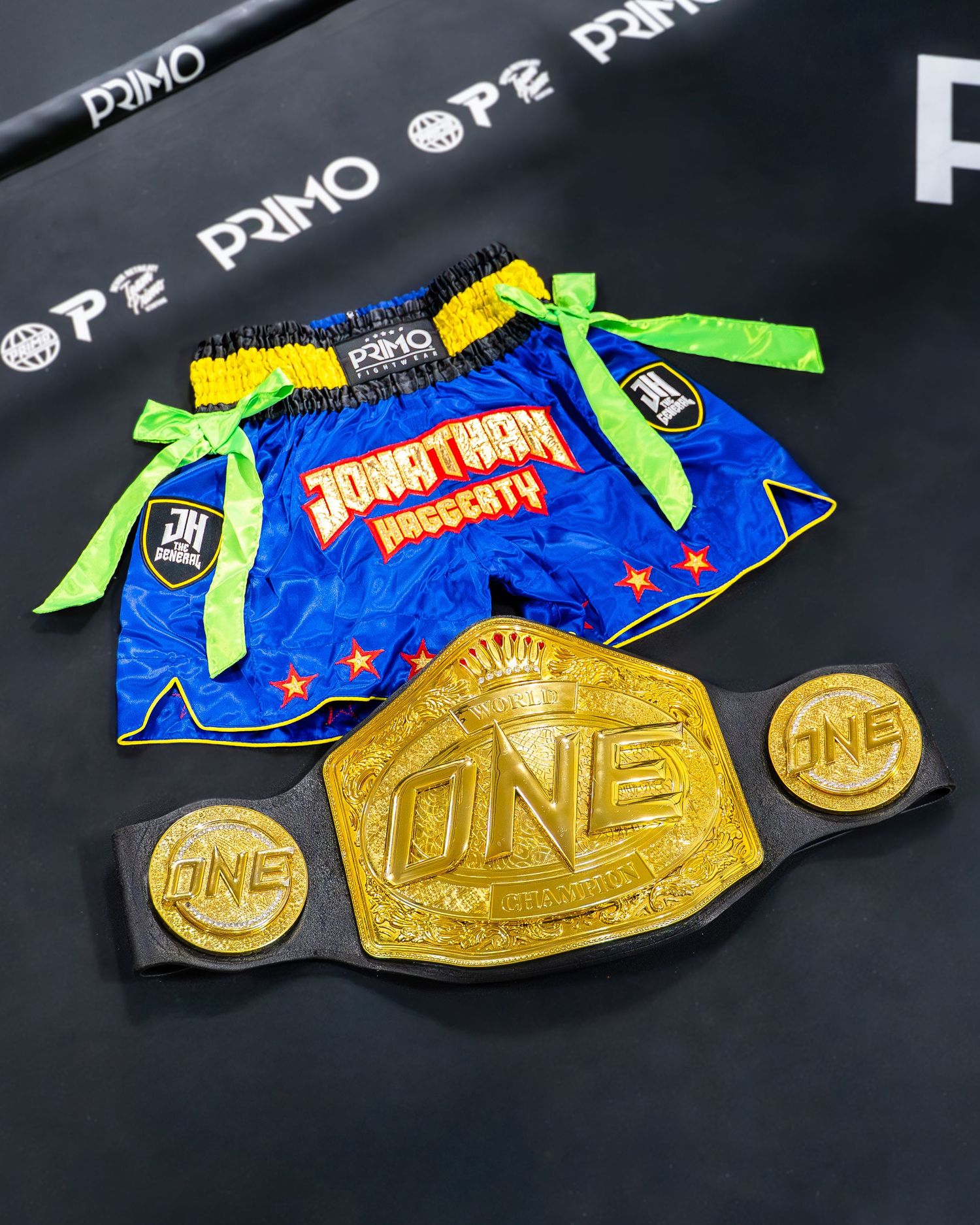 Gold championship medals and blue wrestling singlet with neon green bow displayed on dark background.