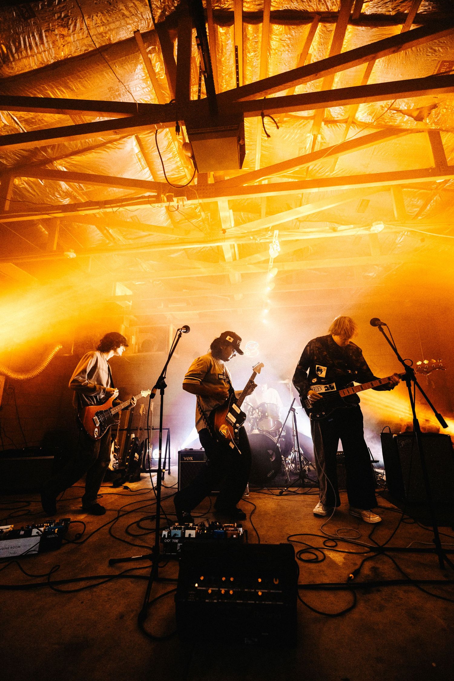 Silhouetted band members perform on stage in dramatic orange lighting during an energetic live music performance.
