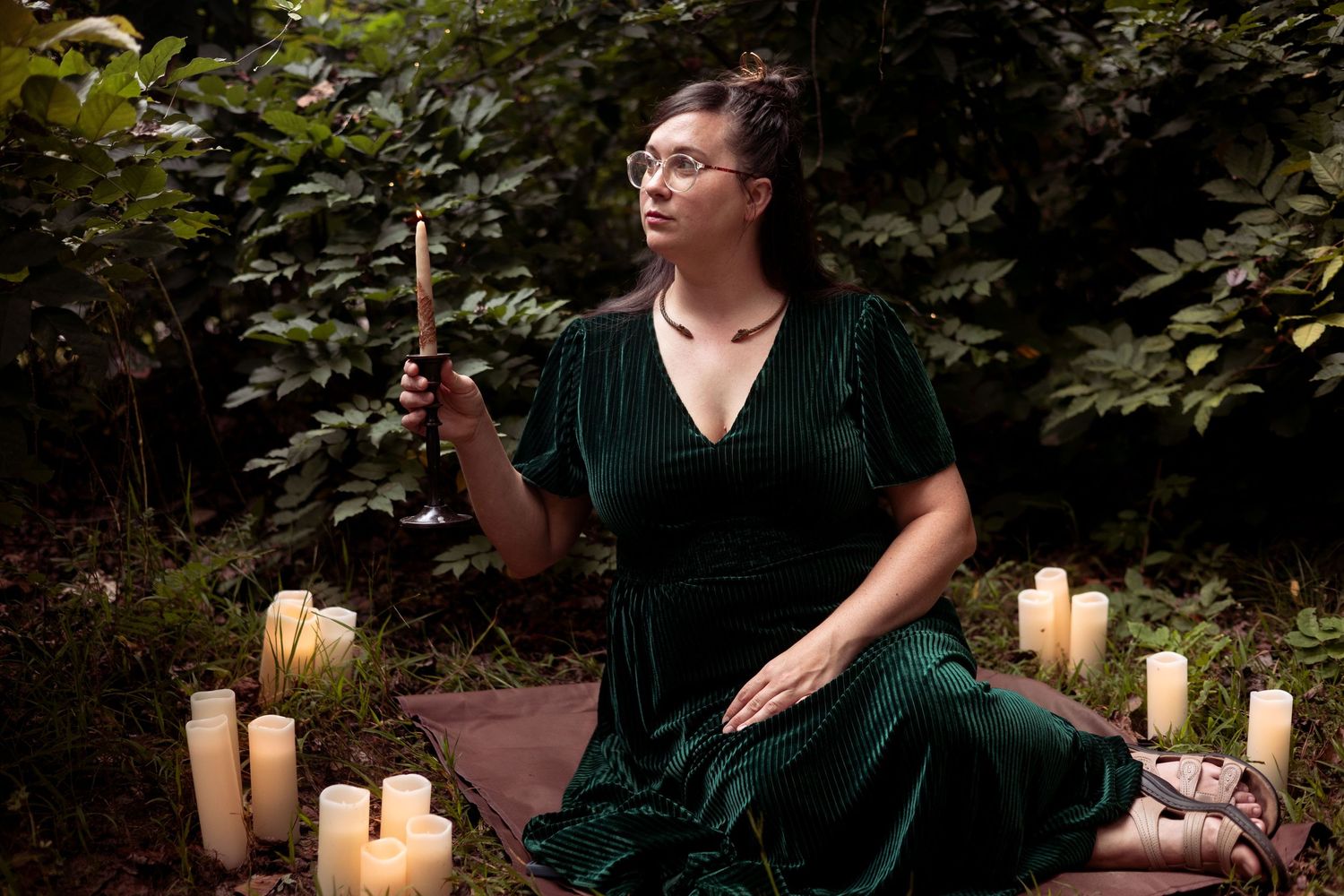 A woman sits on the forest floor surrounded by candles.