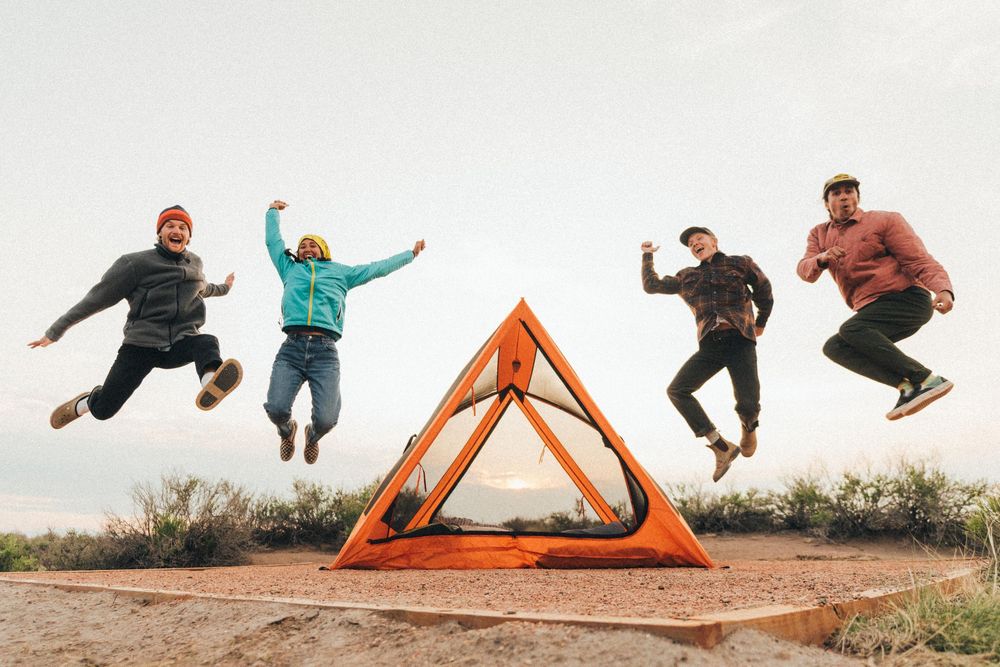 Group jumping sequence photo on rocky terrain with orange tent in background.