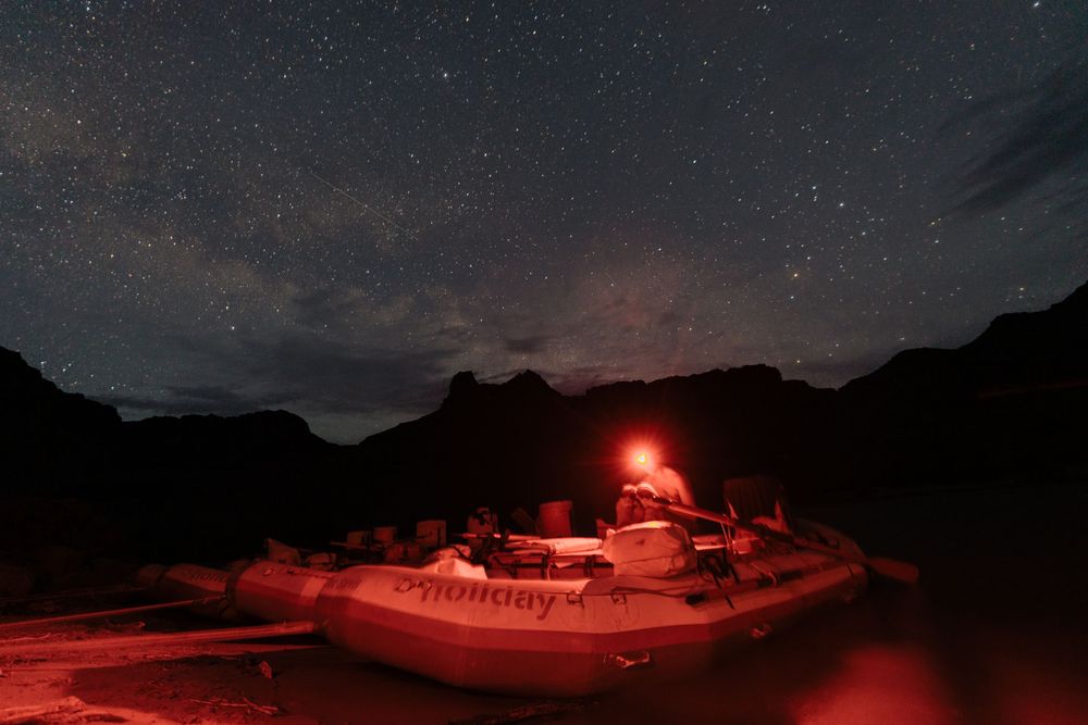 Starry night sky over mountains with red camping lights illuminating the landscape.