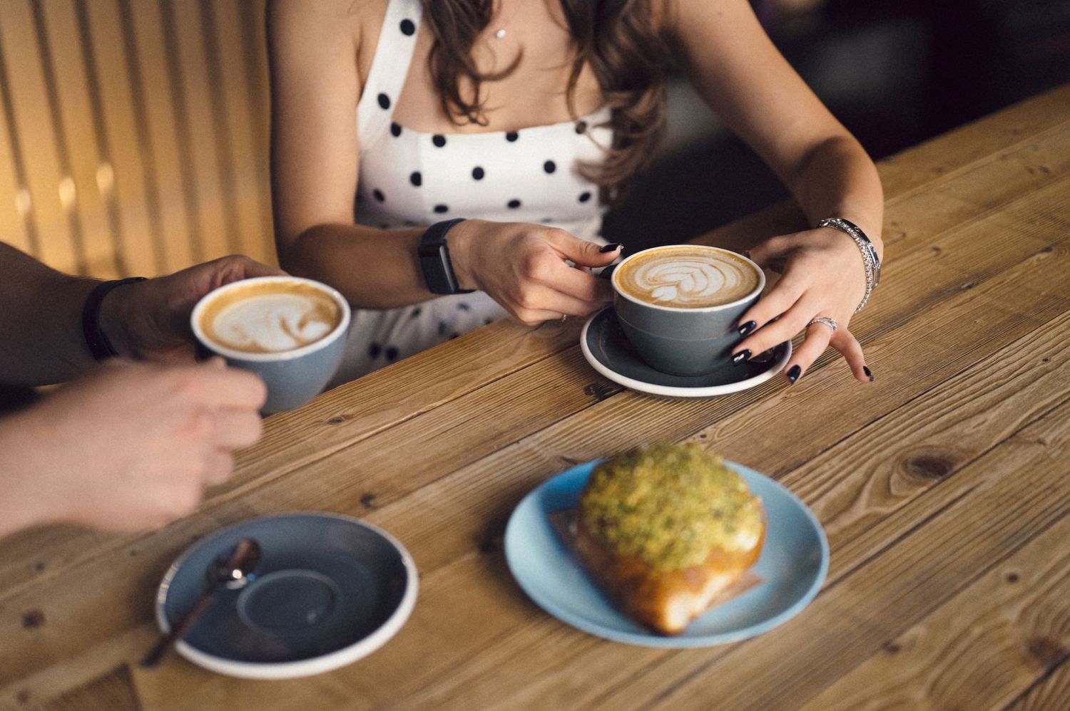 Multiple coffee cups with latte art and pastries on a rustic wooden table at a cafe.