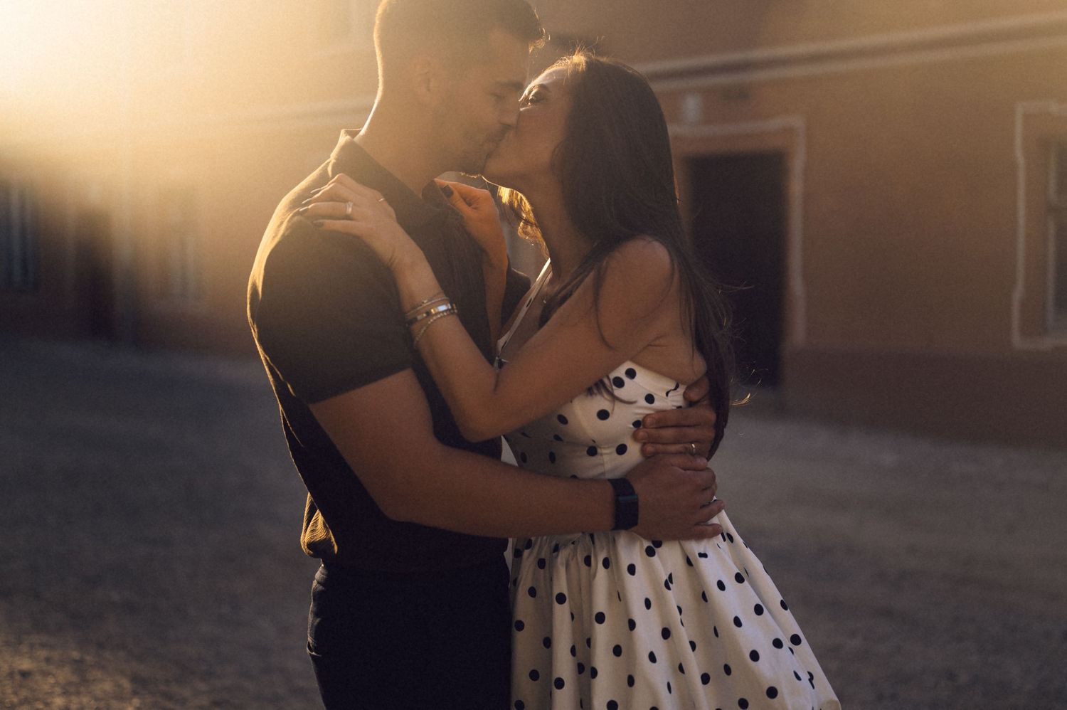 A couple in formal attire dances together during sunset in a romantic outdoor setting.