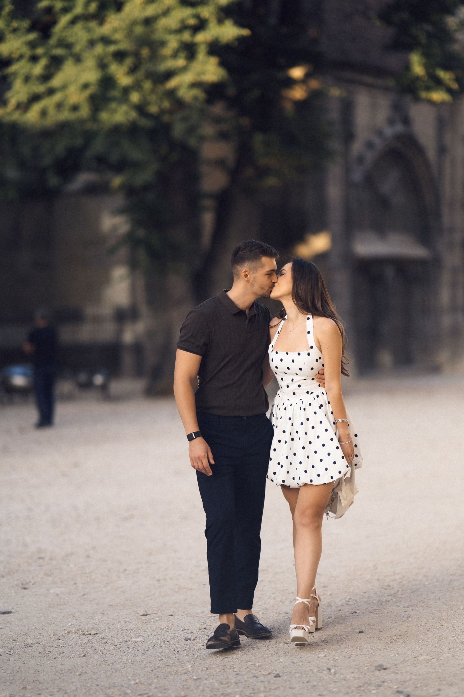 A couple in contrasting black and white outfits share an intimate moment on a sandy path.