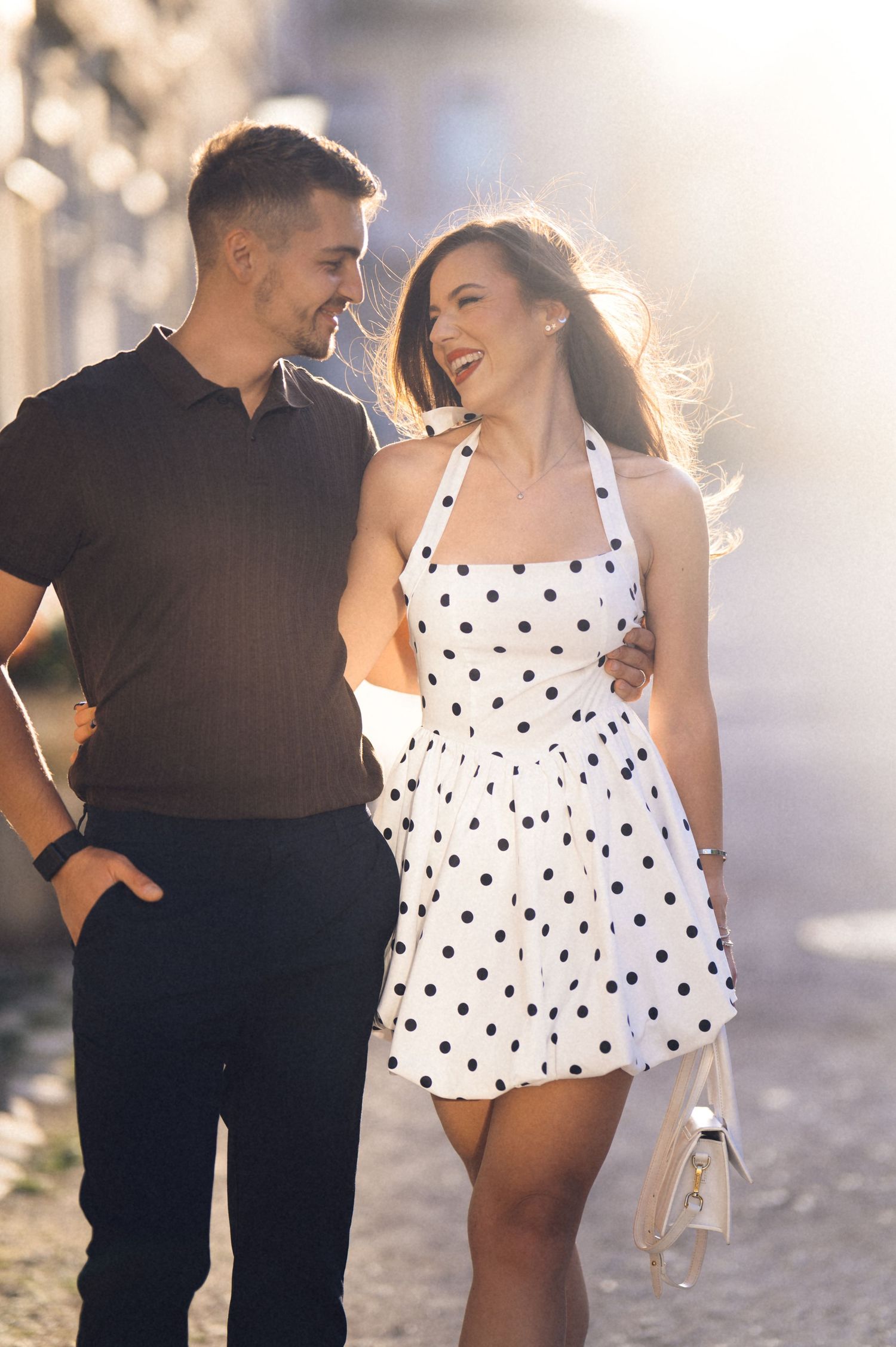 A couple shares a romantic moment outdoors in sunlight, with the woman wearing a polka dot dress.