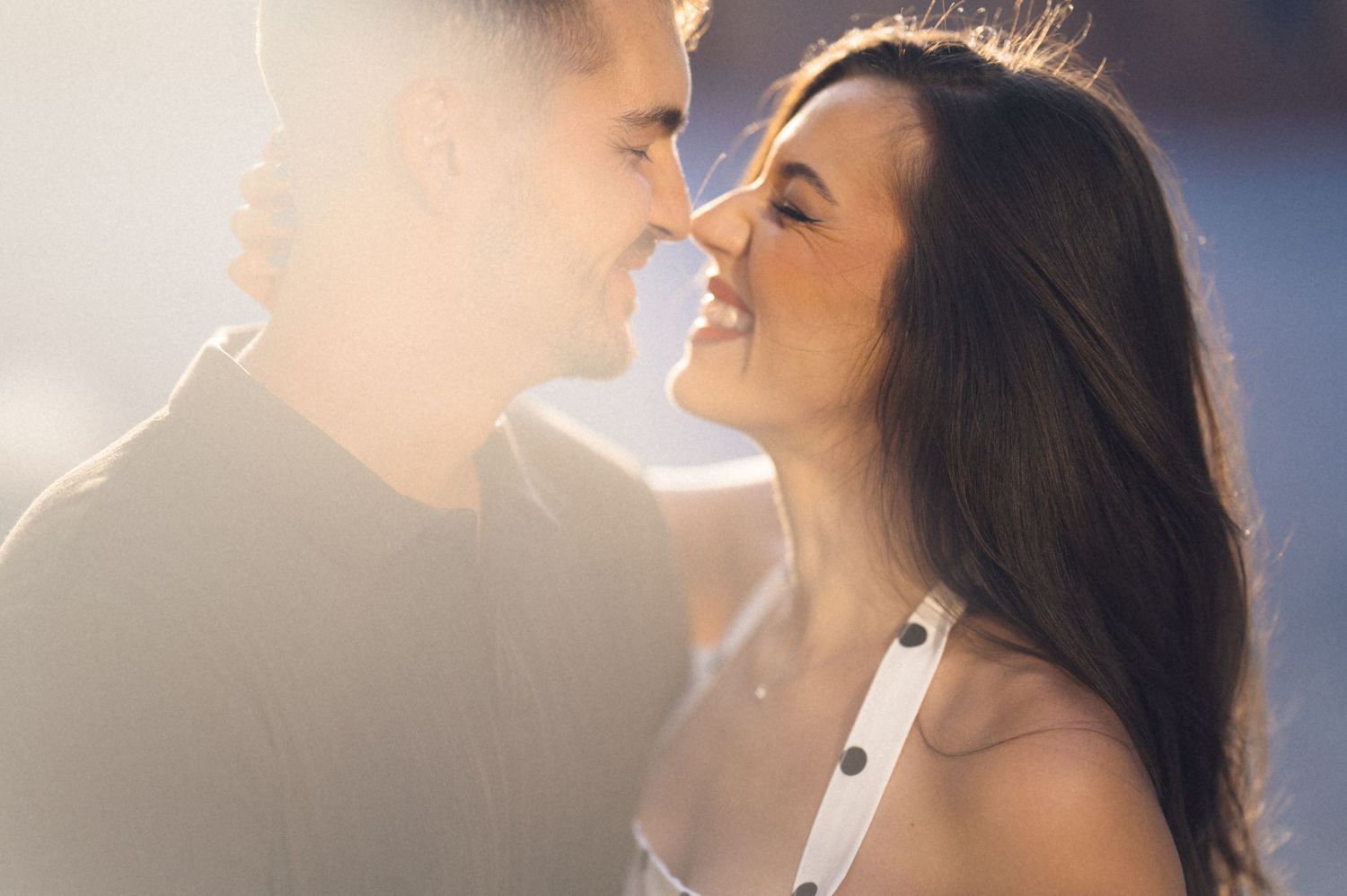 A romantic couple in soft lighting share an intimate moment together as they smile and lean in close to each other.